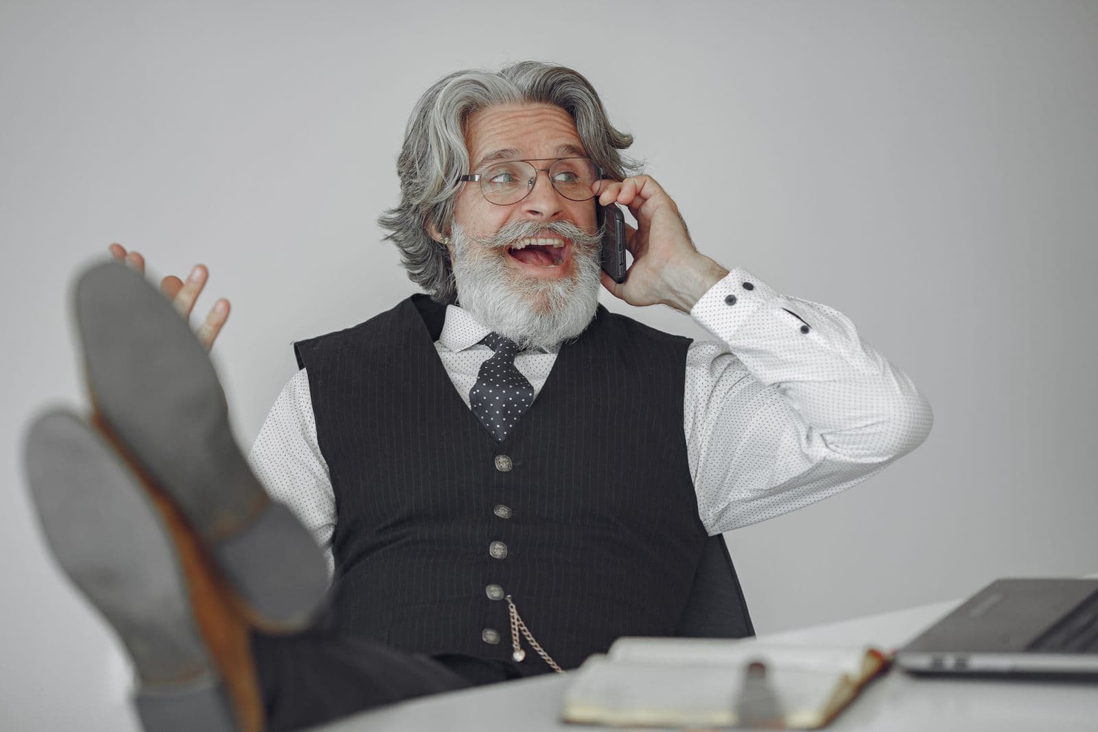 A gray-bearded man with his feet up on his desk