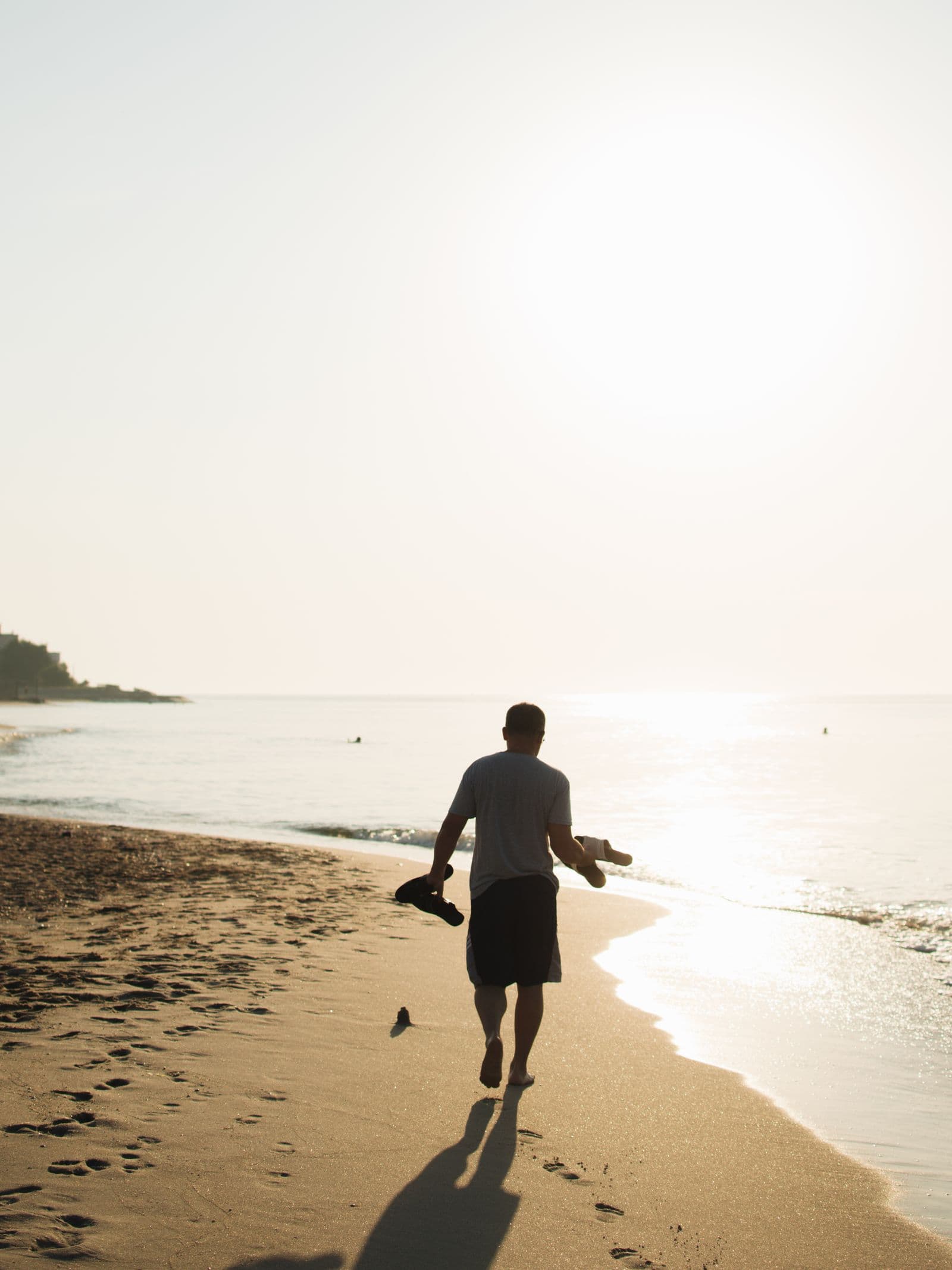A man walking the tide line at sunrise, shoes in hand