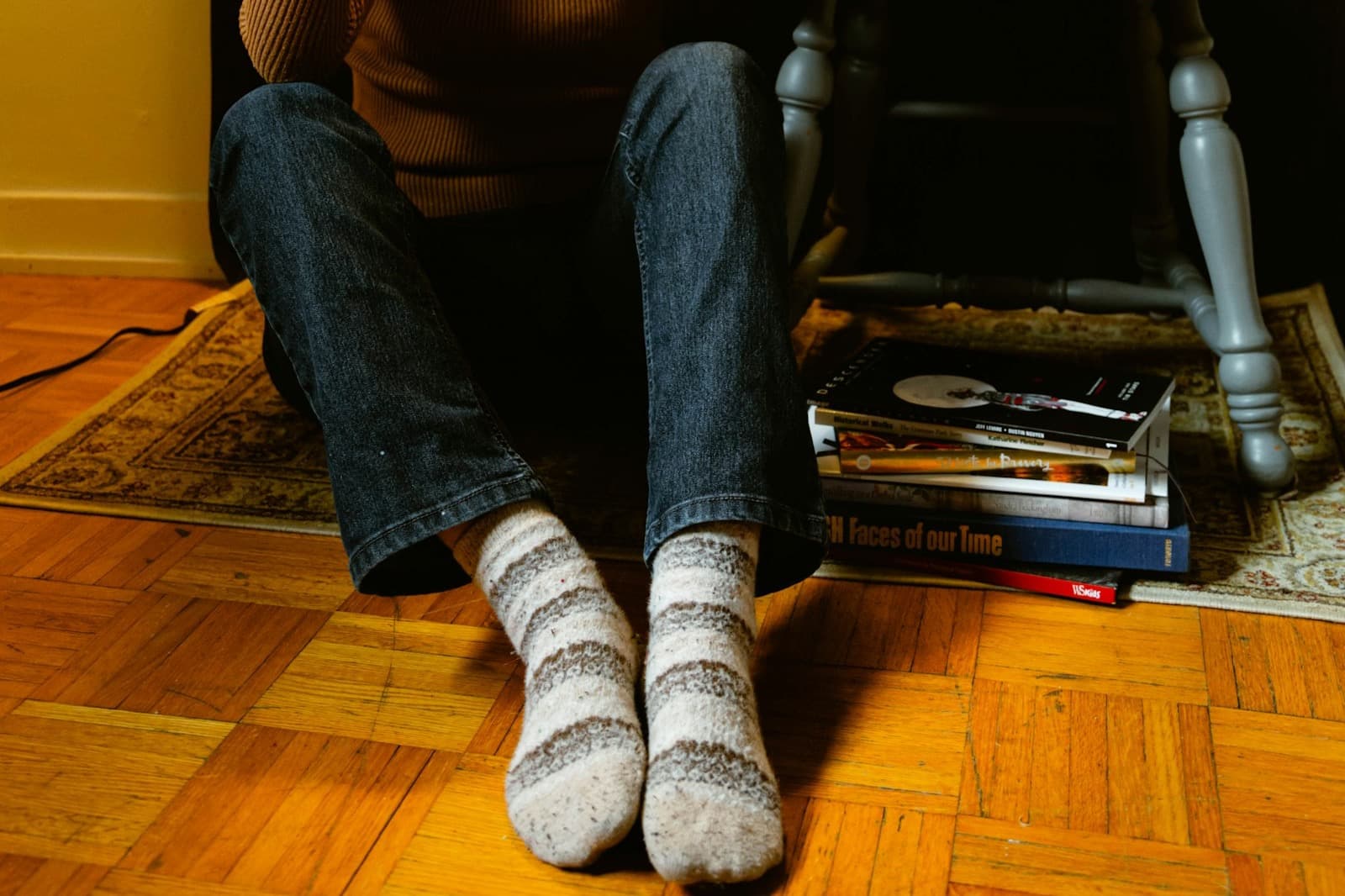 A man in socks sitting on the floor with a book and a mug