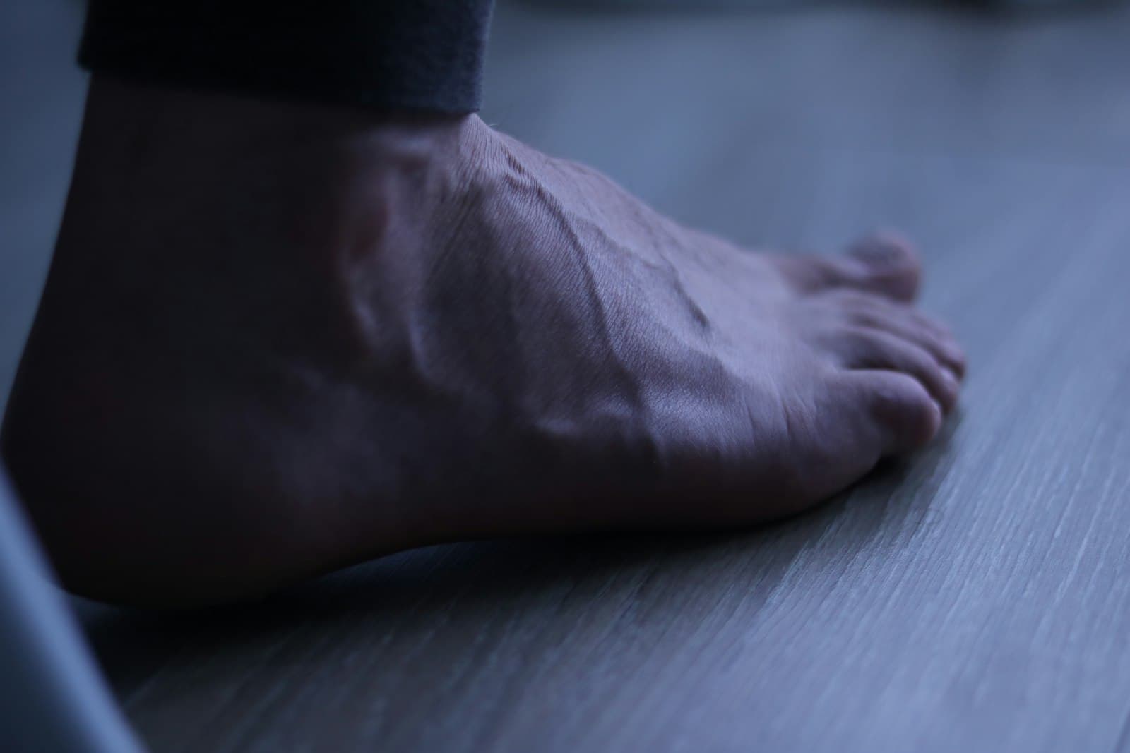 A man's feet resting on a wooden dock, toenails in view