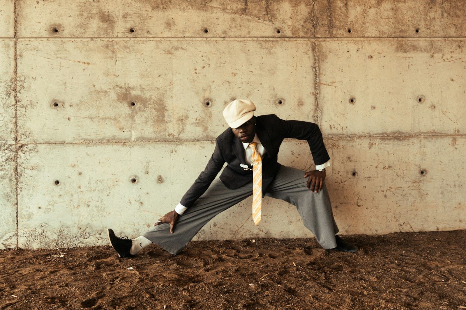 A man in a suit stretching his calf against a concrete wall