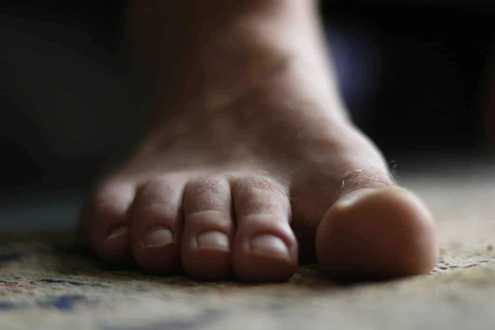 A man's bare foot on the floor, toes in focus